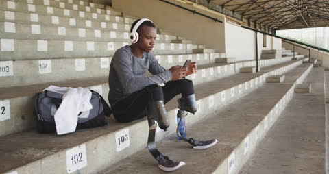 Disabled Athlete Relaxing with Smartphone and Headphones on Stadium Steps