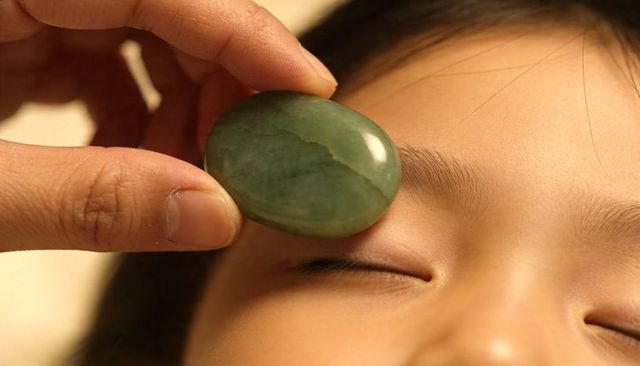 Pressing jade stone on child eyelid for soothing facial relaxation and wellness