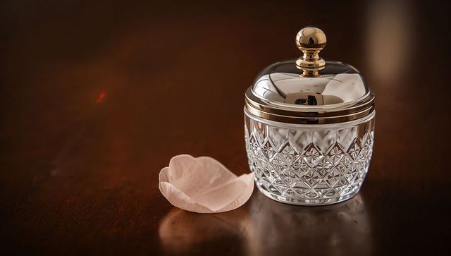 Cut-crystal jar reflecting on dark wood resting beside pale pink petal
