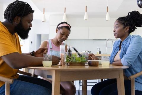African family sharing salad at modern sunlit kitchen table in minimalist open-plan home