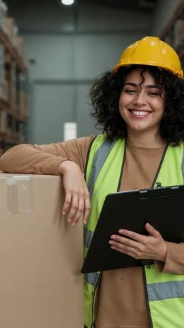 Vertical video Warehouse worker wearing hard hat and safety vest checking inventory with clipboard