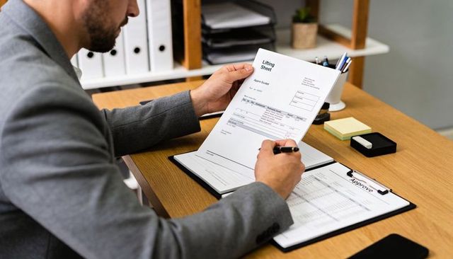 Businessman reviewing and signing lifting sheet at office desk