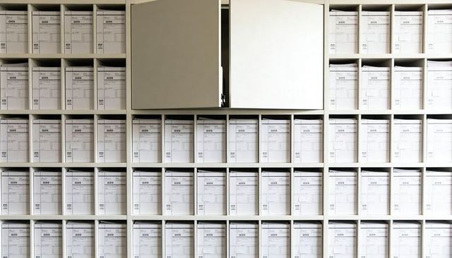 Modular archival shelving holding labeled white records boxes with ajar cabinet door