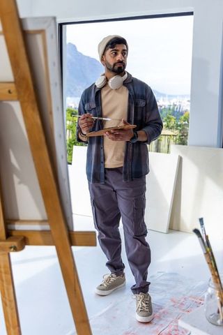 Indian artist painting in sunlit studio wearing beanie and headphones