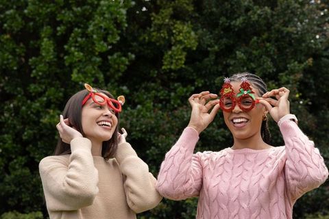Multicultural friends laughing wearing holiday novelty glasses and cozy sweaters outdoors