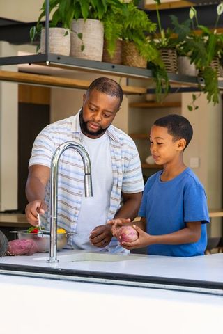 African american father washing vegetables with son at kitchen teaching healthy cooking