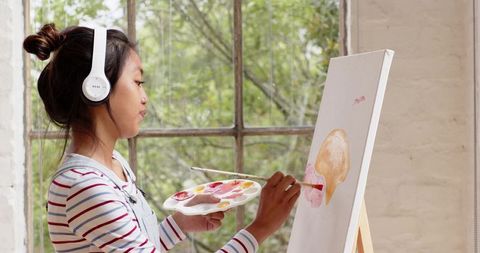 Asian Woman Painting on Canvas with Headphones