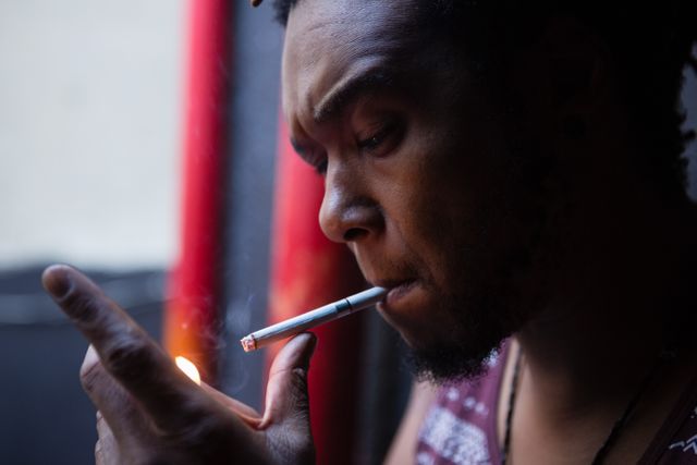 Close-up of a man lighting a cigarette at the entrance of a bar. Ideal for use in articles or campaigns related to smoking, urban lifestyle, relaxation, or nightlife. Can also be used in discussions about health, addiction, or personal habits.