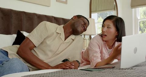 Interracial Couple Collaborating on Wedding Plans with Laptop in Cozy Bedroom