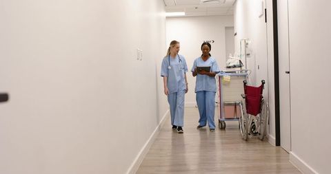 Female nurses walking and discussing patient chart in modern hospital corridor