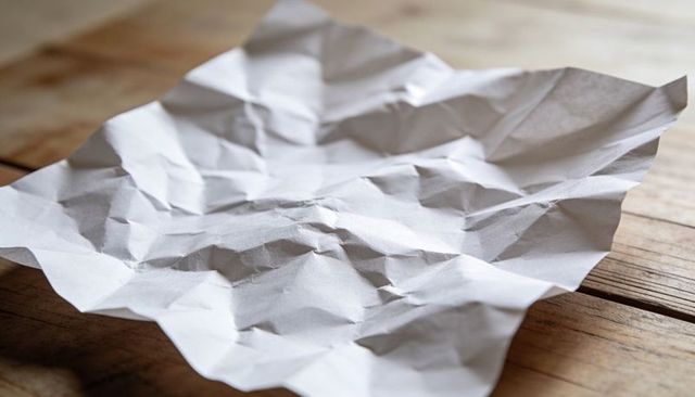 Crumpled White Paper on Rustic Wooden Table Casting Soft Window Light and Shadows