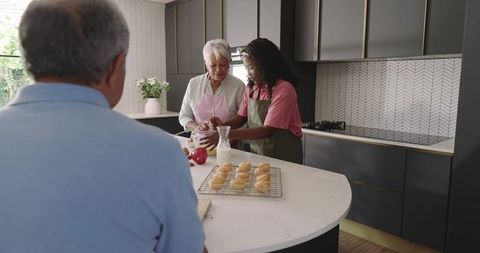 Multigenerational Baking Moment: Senior Woman Teaching African American Woman Mixing on Modern Islan