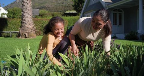 Mother daughter gardening together on sunny suburban lawn teaching planting and bonding