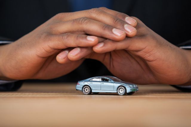 Businessman shielding toy car with hands demonstrates concept of car insurance, protection, and security. Useful for advertisements related to automotive insurance, financial services, security services, and business protection strategies.