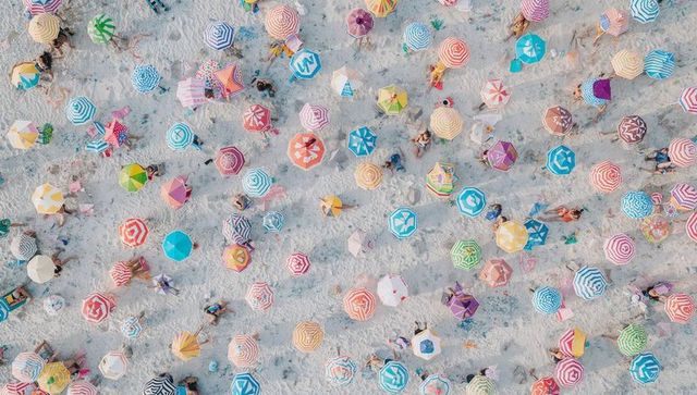 Aerial capturing colorful beach umbrella pattern on sandy shore with sunbathers and shadows