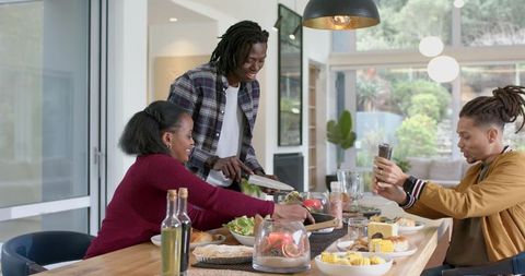 Diverse Friends Serving Dinner at Rustic Dining Table While Capturing Moment on Phone
