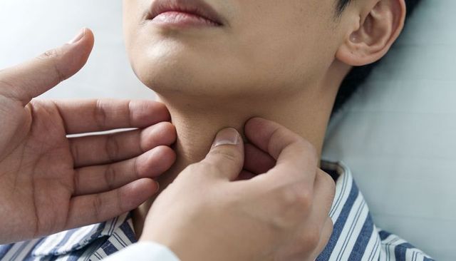 Doctor palpating neck of teen patient during throat and lymph node clinical examination
