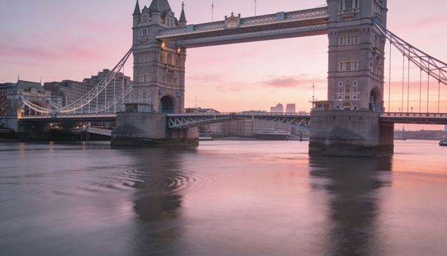 Tower bridge glowing at dusk over river thames with pink sunset reflections