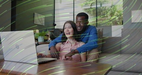 Couple cuddling on couch while browsing laptop together in bright cozy modern living room