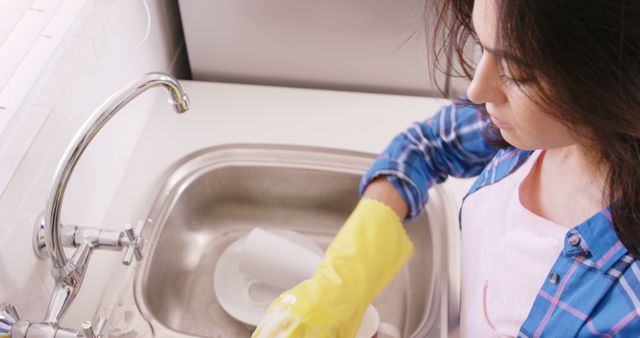 Young woman washing dishes in kitchen sink wearing yellow gloves - Download Free Stock Images Pikwizard.com