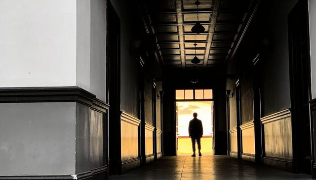 Silhouetted man standing at bright doorway in moody coffered corridor at sunset