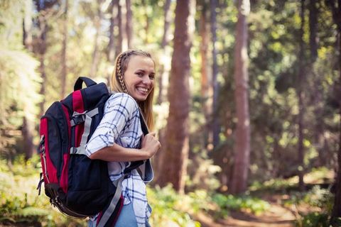 Smiling Woman Hiking Forest Trail with Backpack in Sunny Wilderness