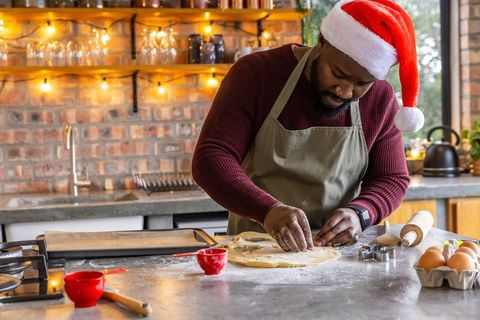 African American man wearing Santa hat baking festive cookies in rustic kitchen