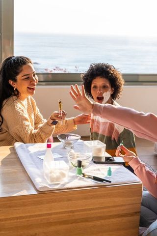 Sunlit coastal family spa moment applying face cream and painting nails together