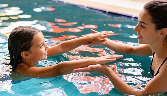 Teen swim instructor teaching child confidence during hands-on pool lesson