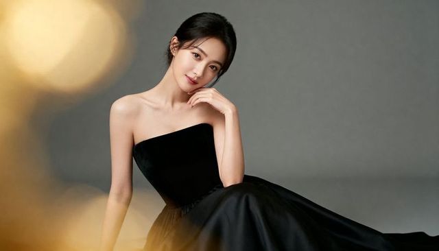 Glamorous asian woman posing in strapless black gown, reclining with warm bokeh lighting