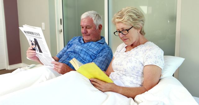 Senior couple reading book and newspaper on bed