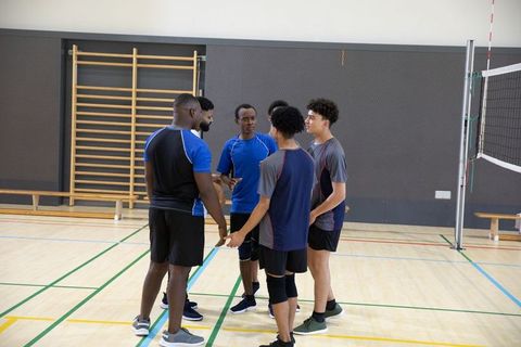 Multiracial male volleyball players huddling for strategy and teamwork on indoor court