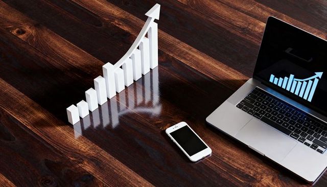 Rising 3d bar chart casting sharp reflections on dark wood desk with laptop and smartphone