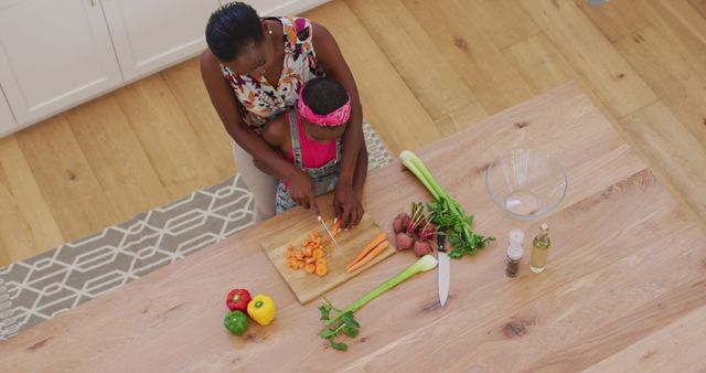 Overhead view of african american mother and daughter chopping vegetables together in the kitchen. family, togetherness and happiness concept