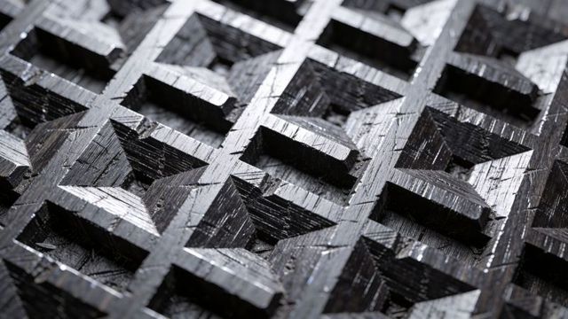 Dark carved wood lattice revealing geometric pyramid pockets and dramatic light highlights