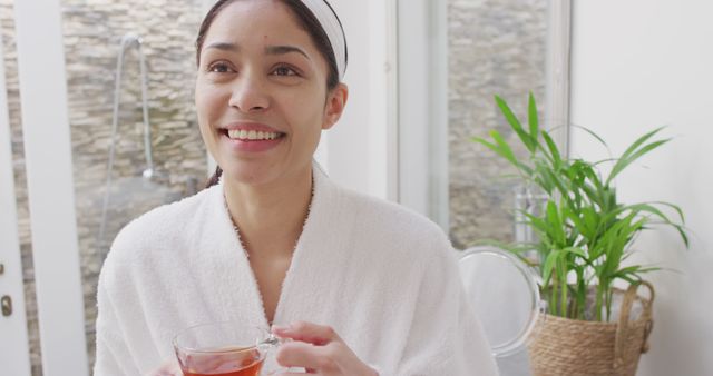 Biracial woman drinking tea and smiling in bathroom. Beauty, health and female spa home concept.