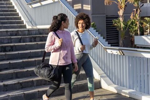 Two women walking urban steps in activewear with duffel bag and water bottle