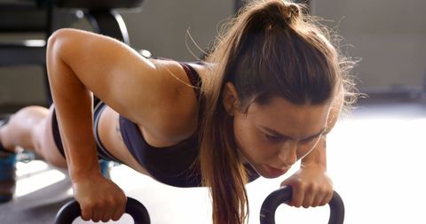Focused woman performing push-ups with fitness gear in studio