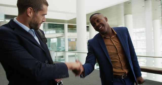 Front view close up of a young African American businessman and a young Caucasian businessman talking as they walk in the corridor of a modern office building and shaking hands before going their separate ways