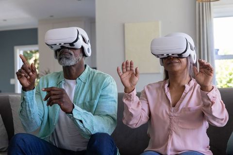 Senior couple exploring virtual reality together at home wearing white vr headsets