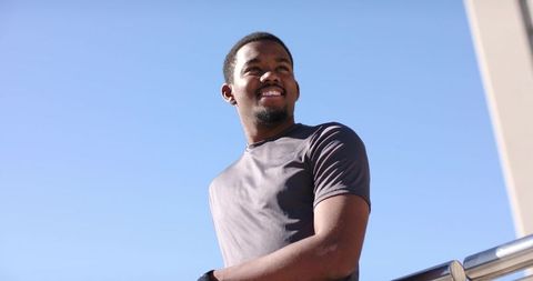 African american man leaning on rooftop railing smiling at sky wearing wristwatch