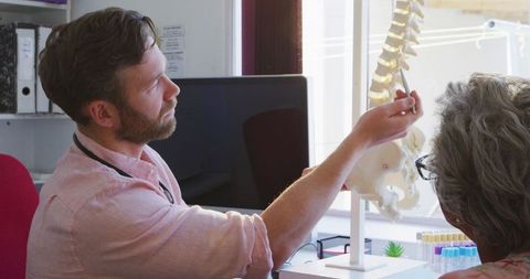 Doctor explaining spine model to elderly patient in clinic
