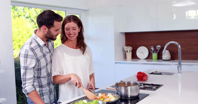 Happy man reaching his wife while she is cooking in the kitchen