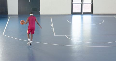 Male Athlete Dribbling Basketball on Indoor Blue Court