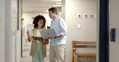 Coworkers Collaborating in Office Corridor with Laptop and Documents