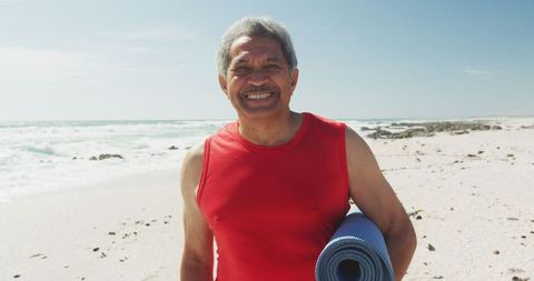 Senior Hispanic Man Smiling on Beach with Yoga Mat