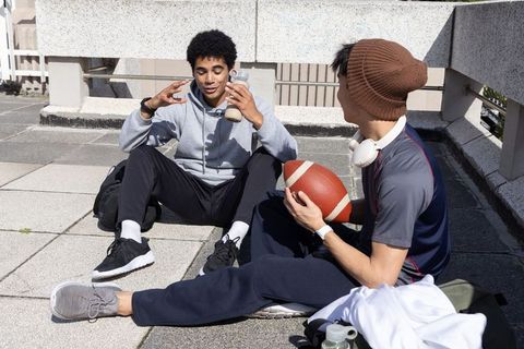 Multicultural teen friends on urban rooftop holding football and bottle casual hangout