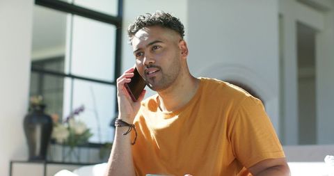 Sunlit african american man talking on smartphone in contemporary minimalist living room