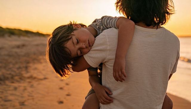 Teen carrying sleeping sibling along golden hour beach at sunset
