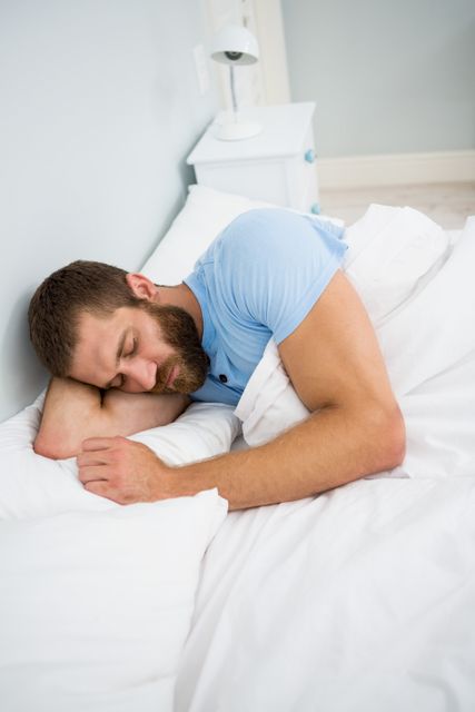 Man sleeping peacefully in bed, resting his head on a pillow. Ideal for concepts of relaxation, sleep, comfort, and home life. Useful for articles or advertisements related to sleep health, bedding products, or lifestyle content.